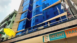 A multi-story building with a modern glass facade, a visible entrance with a metal gate, and a sign for 'Decent Trad' medical equipment and supplies. - Hotel The Grand Hyatt Dhaka (Dhaka)