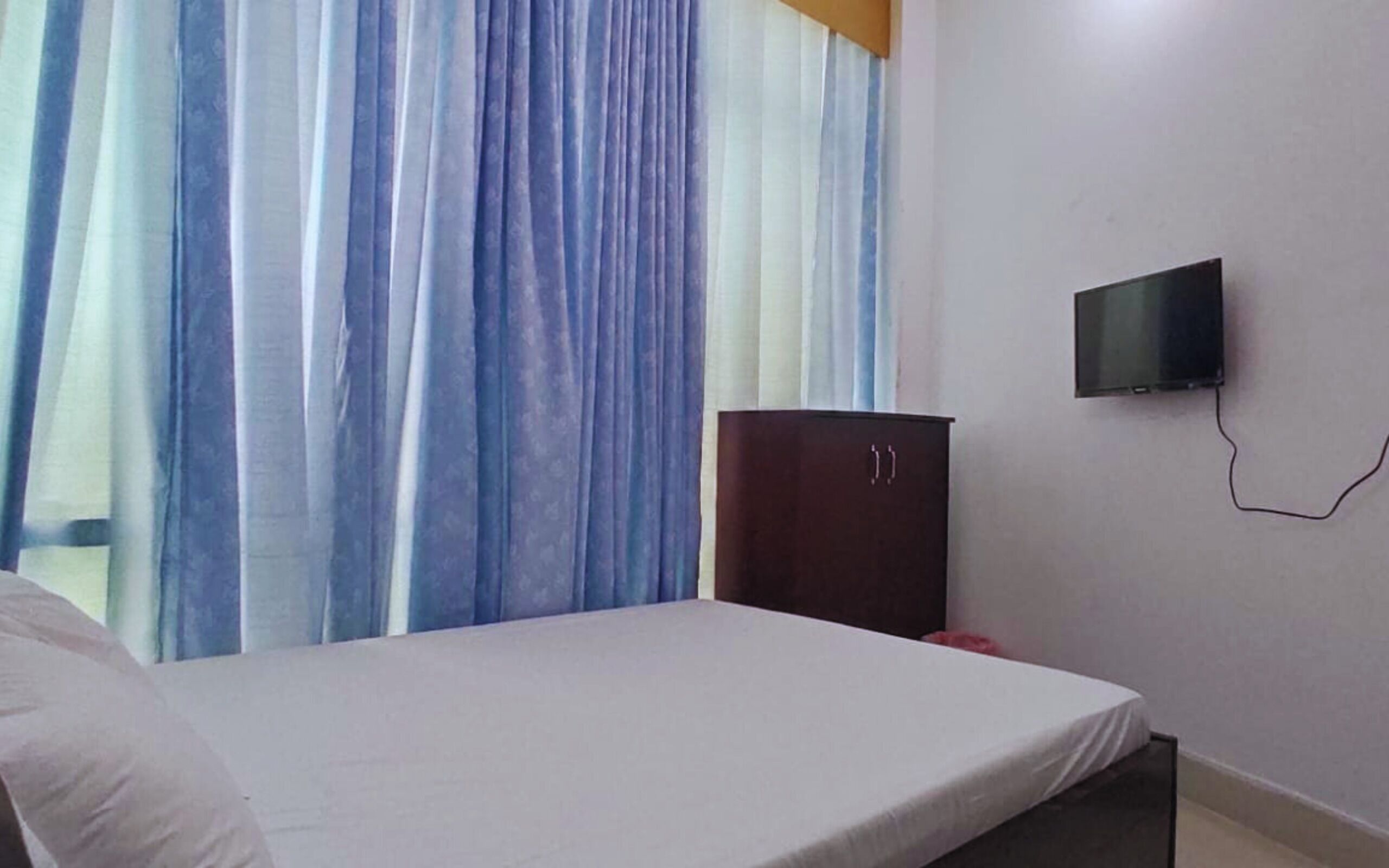 A room with a bed, a TV mounted on the wall, and a wardrobe.