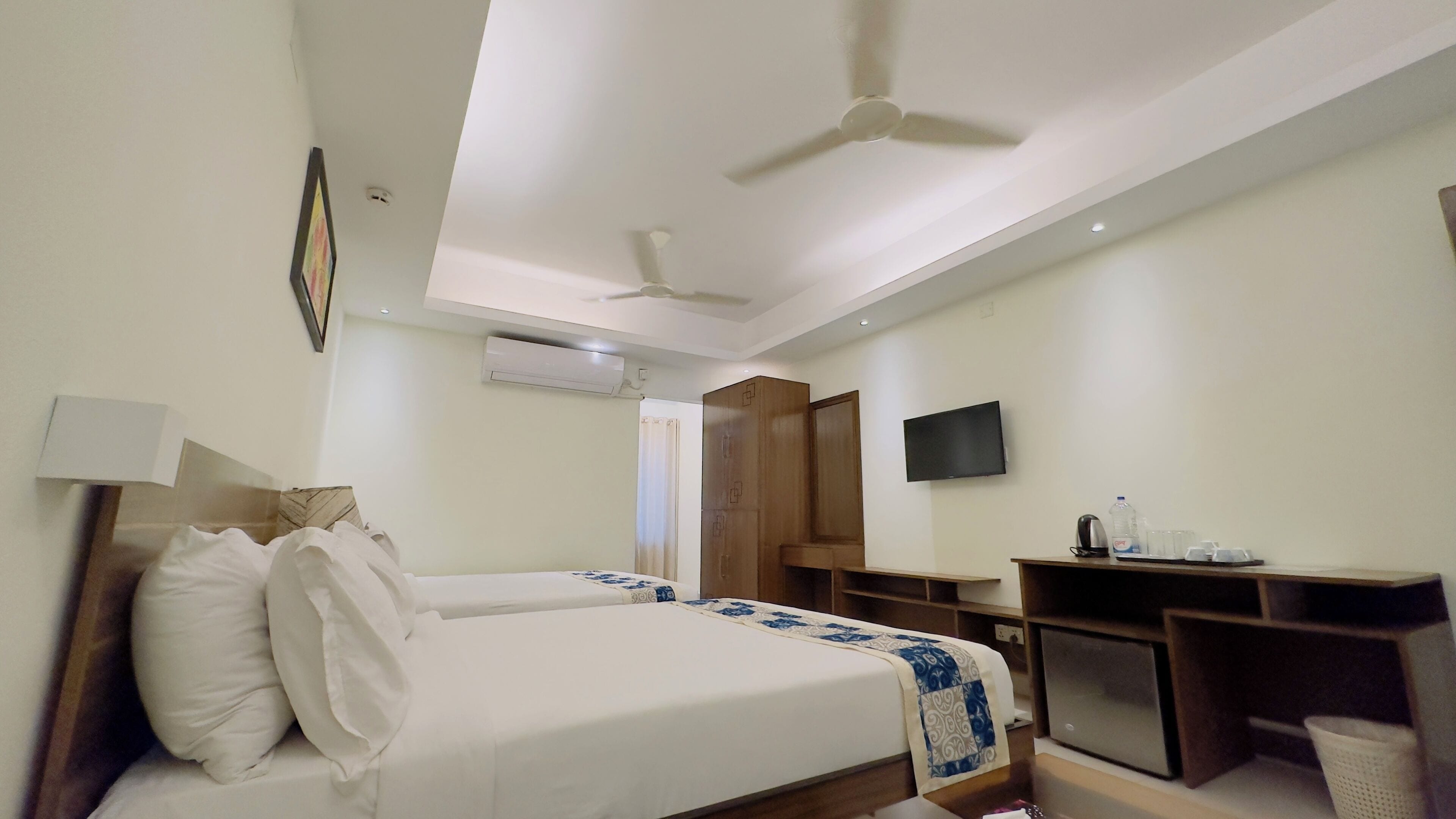 A hotel room with a bed, a desk, a television, and an air conditioning unit.