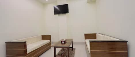 Een kamer met twee houten banken, een kleine tafel en een flatscreen televisie aan de muur.