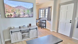 A living room with a TV, a wooden console, a dining area with a table and chairs, and a door. - Campus Casita close to U of A and shopping (Tucson)