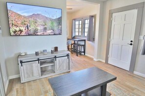 A living room with a TV, a wooden console, a dining area with a table and chairs, and a door. - Campus Casita close to U of A and shopping (Tucson)