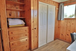 Ein Zimmer mit Holzboden, einem Kleiderschrank, einem Bett mit Kissen, einem Schreibtisch und einem Fenster mit Vorhängen.