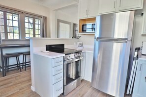 Eine moderne Küche mit Edelstahl-Kühlschrank, Backofen und Mikrowelle. Weiße Schränke und eine kleine Kücheninsel mit Spüle sind vorhanden.