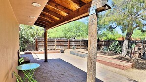 An outdoor patio with a wooden pergola, green metal chairs, and a brick floor. - Pet Friendly Catalina Haven (Tucson)
