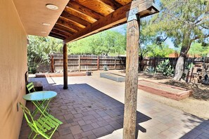 En uteplats med en träpergola, gröna metallstolar och ett tegelgolv.