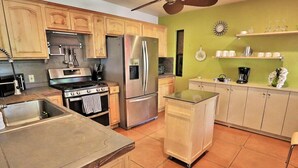 A kitchen with wooden cabinets, stainless steel appliances, a tiled floor, and a green accent wall. - Pet Friendly Catalina Haven (Tucson)