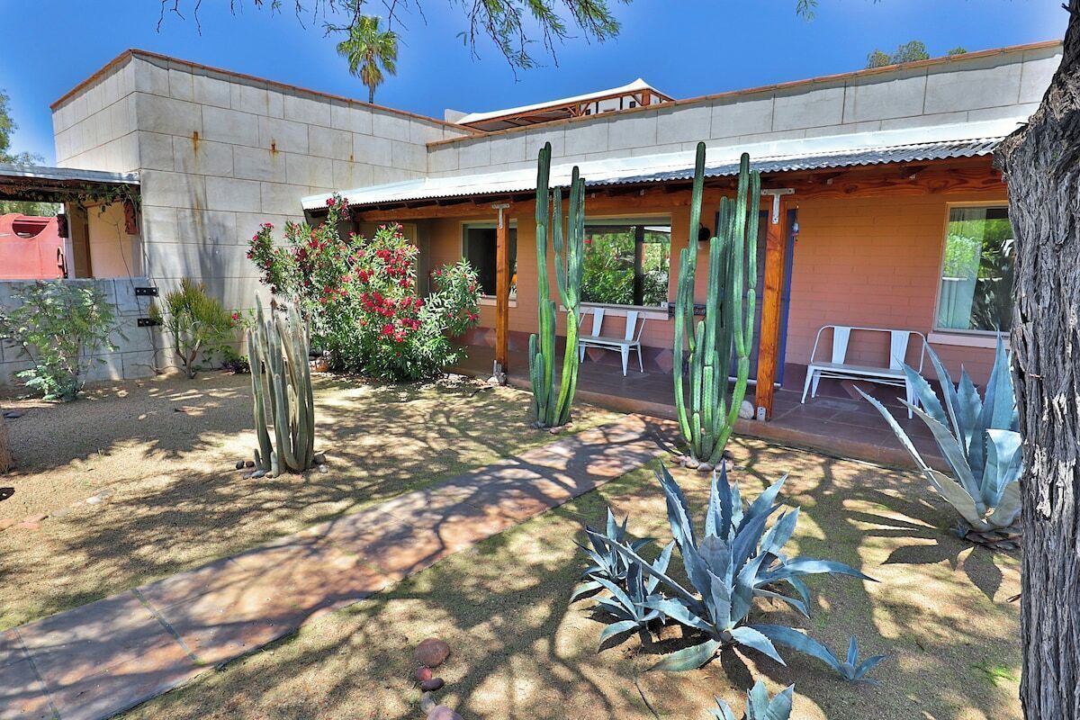 Un bâtiment doté d’un patio agrémenté de cactus et de plantes d’agave, d’un espace salon couvert et offrant une vue sur un ciel dégagé.
