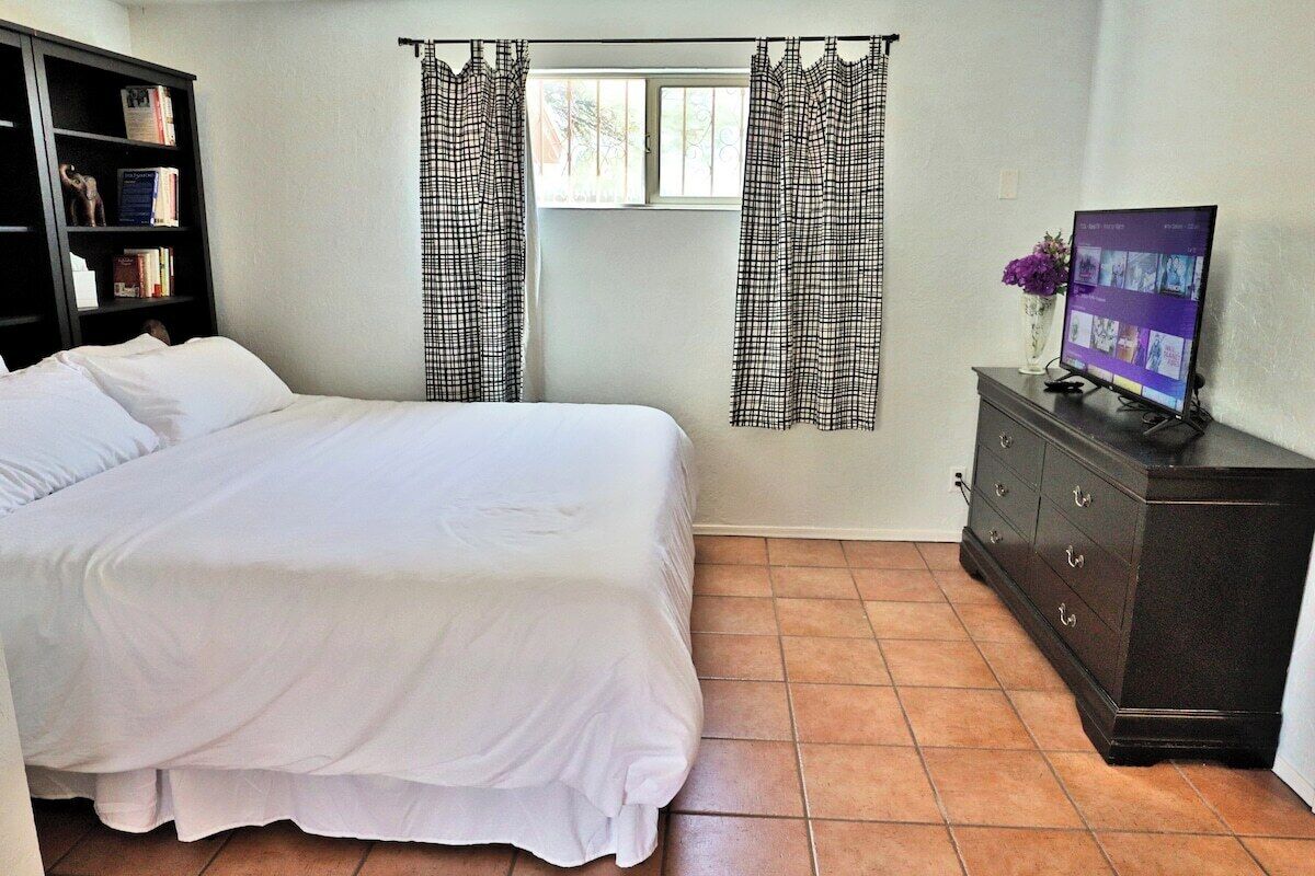 A bedroom with a bed, a dresser, a television, and a window with curtains.