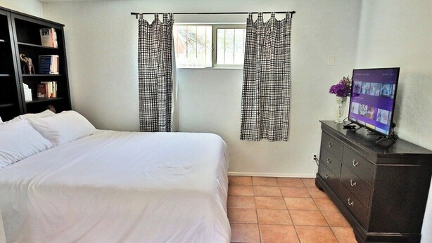 A bedroom with a bed, a dresser, a television, and a window with curtains. - Pet Friendly Catalina Haven (Tucson)
