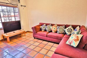 A living room with a sofa, colorful cushions, a wooden bench, and a television.