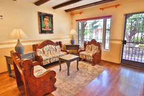 A living room with wooden furniture, a sofa, two armchairs, a coffee table, and a painting on the wall.