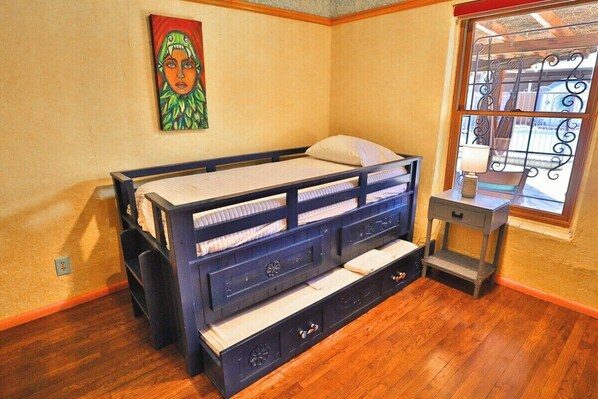 A room with a bed, a small table, and a window with decorative ironwork.