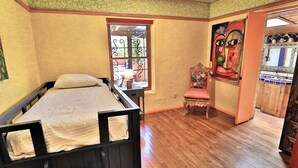 A room with a bed, a chair, a window with decorative iron bars, and a painting on the wall.