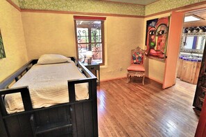 A room with a bed, a chair, a window with decorative iron bars, and a painting on the wall.