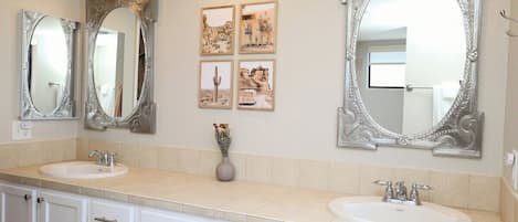 Une salle de bain avec deux lavabos, un grand miroir décoratif et quatre tableaux encadrés accrochés au mur.
