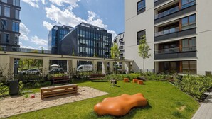 A modern outdoor courtyard with a wooden bench, a unique orange sculpture, and a paved walkway. - ShortStayPoland Zdziechowskiego B152 (Warsaw)