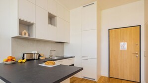 A modern kitchen with white cabinets, a black countertop, a toaster, and a bowl of fruit. - ShortStayPoland Zdziechowskiego B152 (Warsaw)