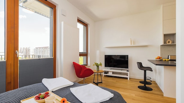 A modern hotel room with a bed, a TV, a small kitchen area, and a balcony with a view of buildings. - ShortStayPoland Zdziechowskiego B152 (Warsaw)