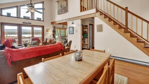 A spacious living area with a wooden dining table, a red blanket on a sofa, and a staircase leading to an upper level. - Lakefront | Private Dock | Family Friendly | Kayaks | Hot Tub | Row Boat | Fireplace (Lake Ariel)