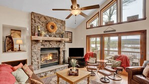 A cozy living room with a stone fireplace, leather furniture, and a large window overlooking a lake. - Lakefront | Private Dock | Family Friendly | Kayaks | Hot Tub | Row Boat | Fireplace (Lake Ariel)