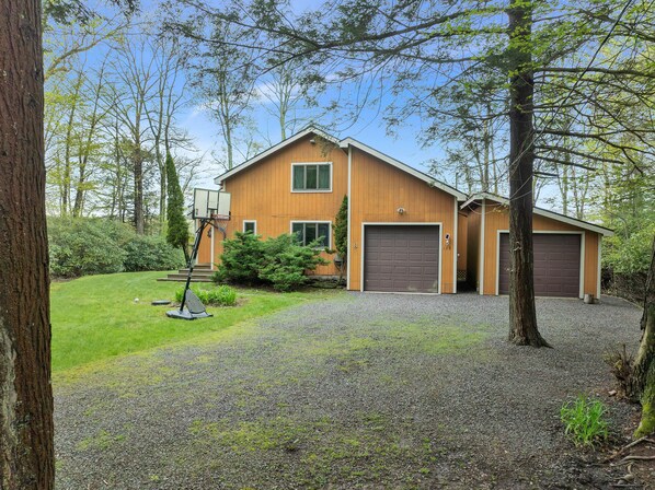 A two-story wooden house with a front garage, a basketball hoop, and a well-maintained lawn.