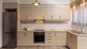 A modern kitchen with light wood cabinets, a stainless steel refrigerator, an oven, and a sink.