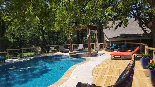 A backyard with a swimming pool, wooden deck, lounge chairs, and a hammock.