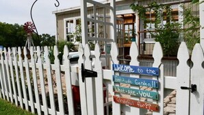 A white picket fence with a windmill and a house with a sign that reads "Welcome to the Gratitude Garden!! What are you grateful for??"
