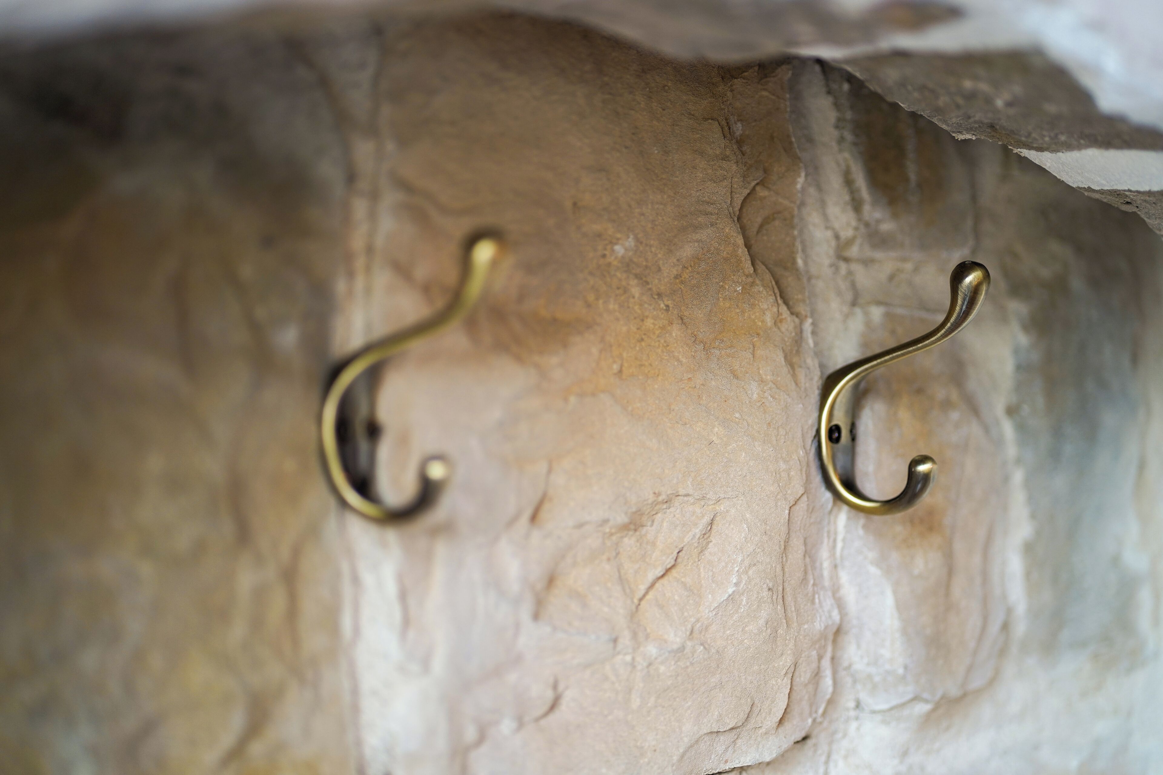 Two brass hooks on a textured wall.