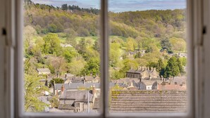 A view through a window of a town with buildings and a forested hill. - The Coach House : Cosy Cottage Retreat (Bakewell)