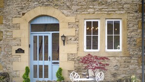 A stone building with a blue door, a sign reading "Coach House Cottage," and a small table with chairs outside. - The Coach House : Cosy Cottage Retreat (Bakewell)