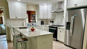 Una cuina moderna amb armaris blancs, un frigorífic d'acer inoxidable, un forn de bola i una illa central amb un plat de fruita.