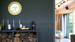 Un intérieur moderne agrémenté d’un luminaire circulaire fixé au mur, d’une étagère avec des bougies, d’une lanterne et d’une pile de bois de chauffage.
