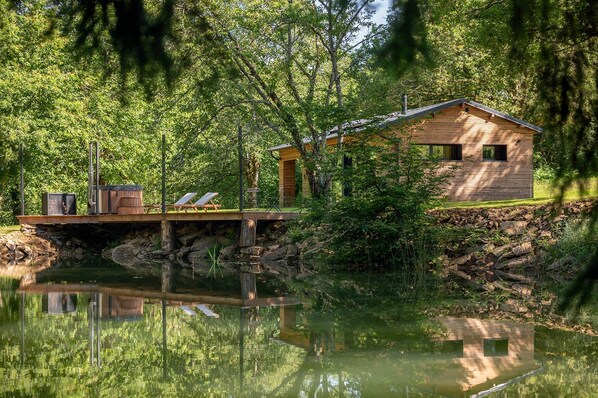 Una cabaña de madera junto a un lago, con una terraza y un bote pequeño.