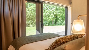 Une chambre avec une grande fenêtre, un lit agrémenté d’oreillers à motifs et une lampe de chevet.