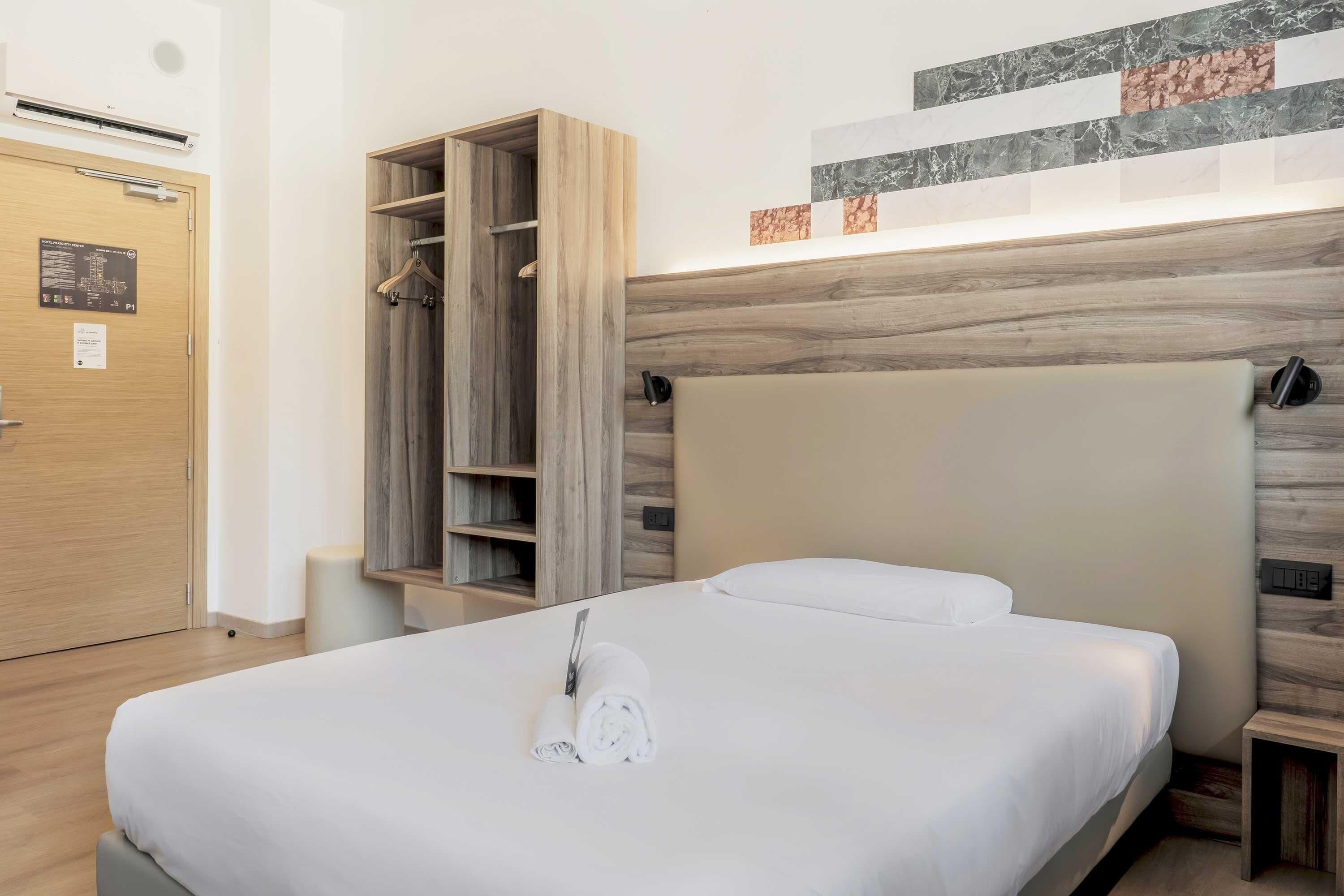 Una camera d'albergo con un letto, un armadio in legno, una mensola a parete e un comodino.