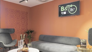 A modern living room with a grey sofa, two armchairs, a marble coffee table, and a decorative plant. A sign on the wall advertises a B&M program. - B&B Hotel Prato City Center (Prato)