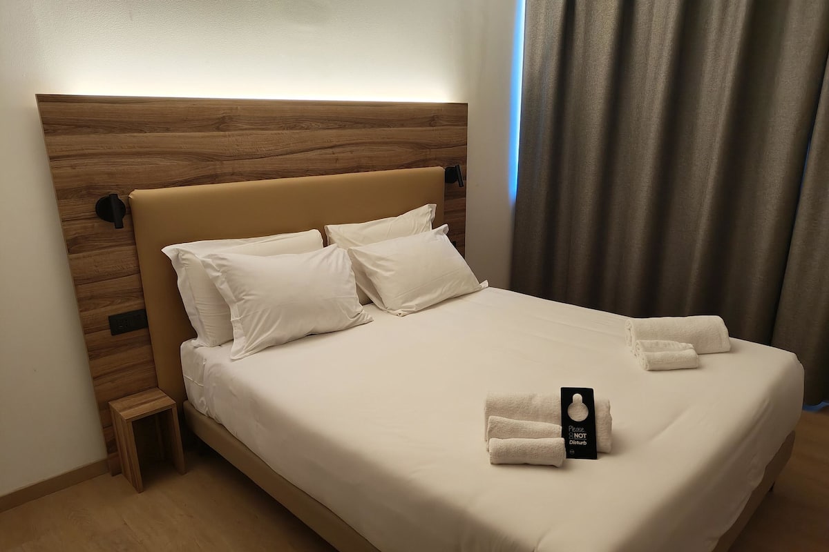 Un lit bien fait, avec du linge de lit blanc et des oreillers, une petite table de chevet et un panneau posé sur le lit.