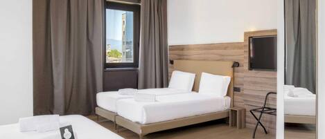 Ein Hotelzimmer mit einem großen Bett, einem kleineren Bett, einem Fernseher und einem Fenster mit Vorhängen.