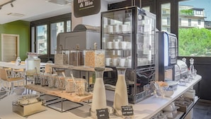 A café counter with a coffee machine, milk dispensers, and a glass display case. - B&B Hotel Prato City Center (Prato)