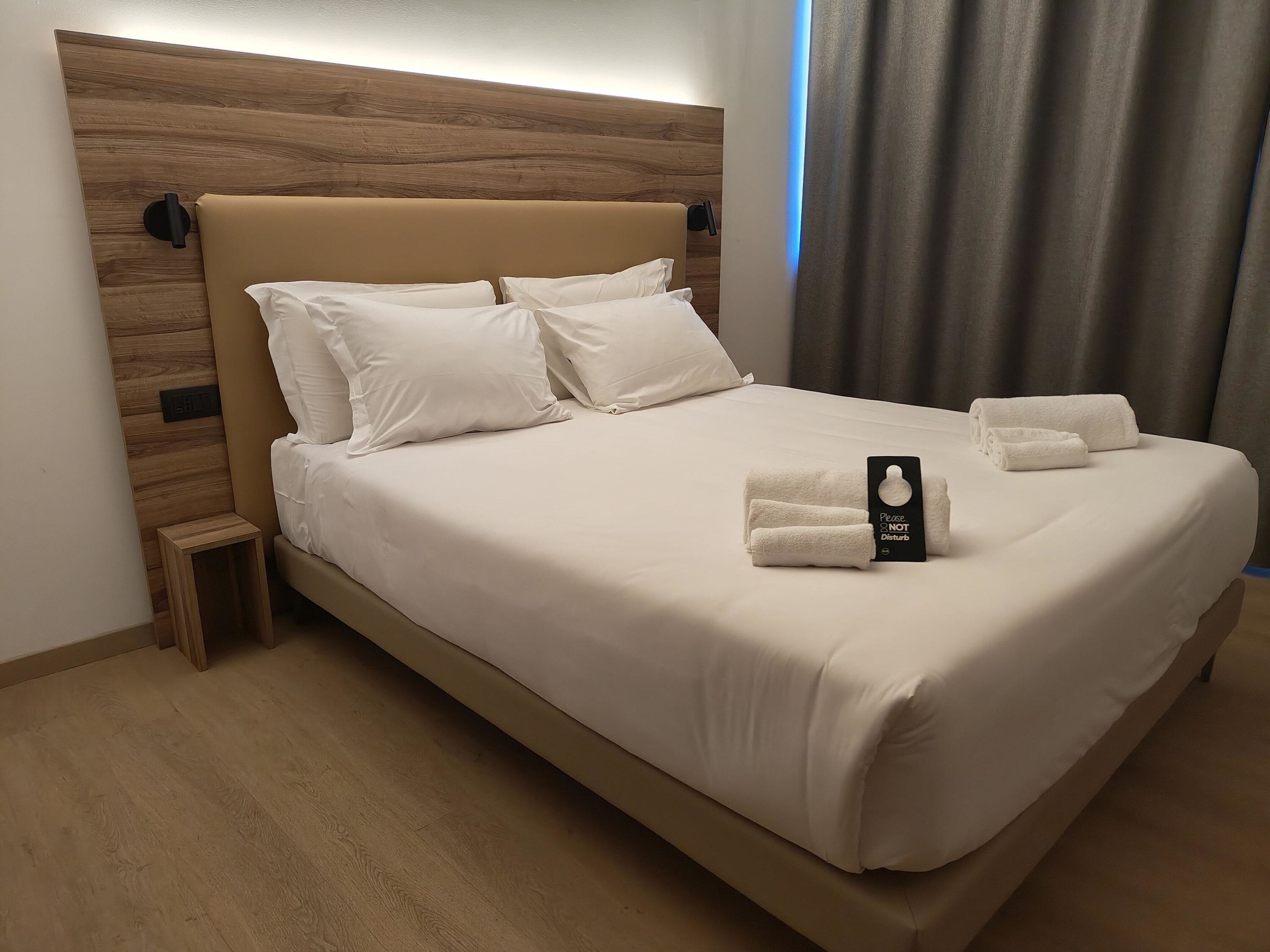 A neatly made bed with white linens and pillows, a small bedside table, and a sign on the bed.