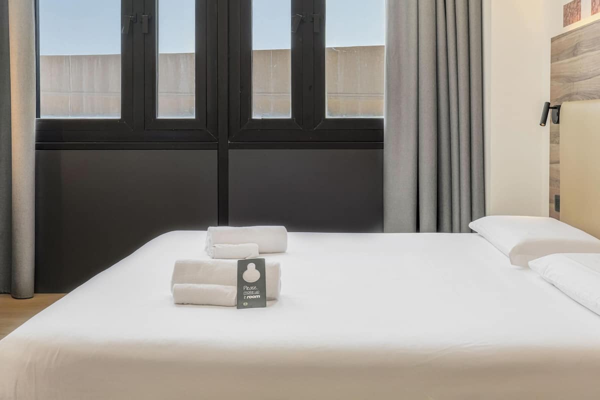 Un lit bien fait, avec du linge de lit blanc, et une pancarte indiquant qu’il s’agit d’une chambre.