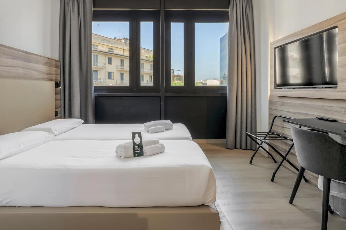 Une chambre d’hôtel avec deux lits, un bureau, une télévision et une vue sur les bâtiments, grâce à de grandes fenêtres.