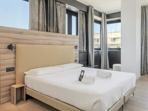Une chambre d’hôtel moderne avec un grand lit, une tête de lit en bois et une vue sur la ville grâce à de grandes fenêtres.