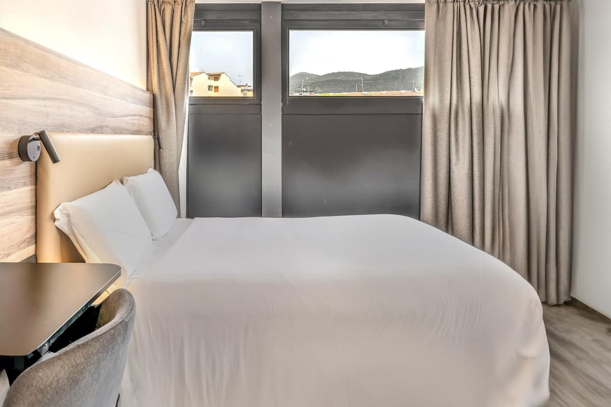 Une chambre d’hôtel avec un lit, un bureau et une fenêtre avec des rideaux.