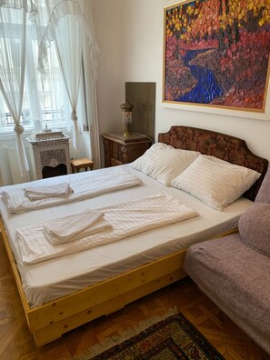 Ein Bett mit weißer Bettwäsche, ein Holz-Kopfteil, ein Nachttisch mit Lampe, ein dekorativer Spiegel und ein farbenfrohes Bild an der Wand.