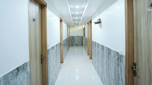 A long, narrow hallway with white tiled floors and marble walls, featuring wooden doors and recessed lighting. - Hotel Aman Inn (New Delhi)