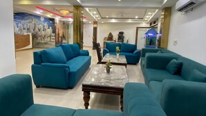 A modern living room with teal sofas, a marble coffee table, and a mural of horses on the wall. - Hotel Aman Inn (New Delhi)
