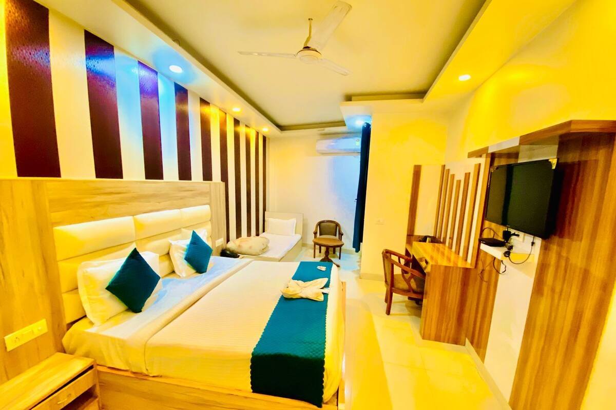 A hotel room with a large bed, a desk, a chair, a TV, and a ceiling fan.